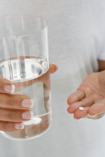 Close-up of woman's hands holding pill and glass of water