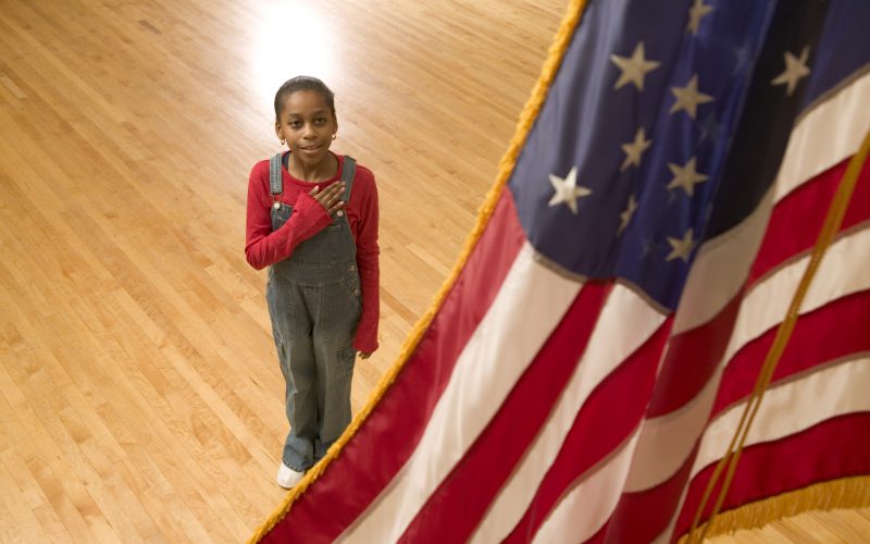 girl beneath flag saying pledge of allegiance